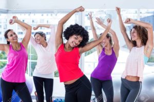 Happy women exercising with arms raised in fitness studio